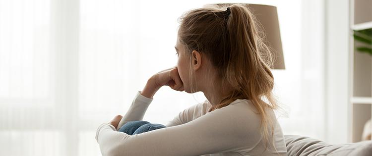 A woman sits on a couch alone in a well lit room.