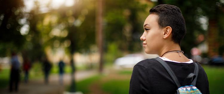 A young person with short hair and a back pack looks off to the side with their head turned.