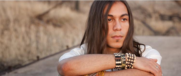 young man sits with arms folded, looking thoughtfully offscreen