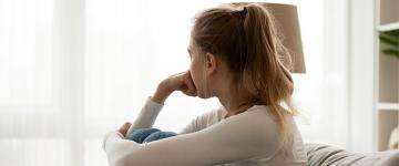 A woman sits on a couch alone in a well lit room.