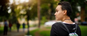 A young person with short hair and a back pack looks off to the side with their head turned.