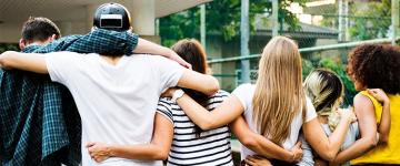 Five people stand with arms linked behind their backs and over their shoulders. The look off into the distance.