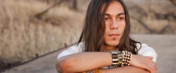 young man sits with arms folded, looking thoughtfully offscreen