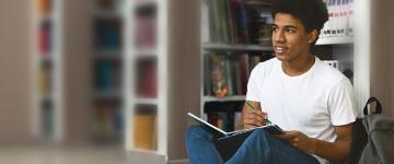 Young man seated in library writing in a notebook.