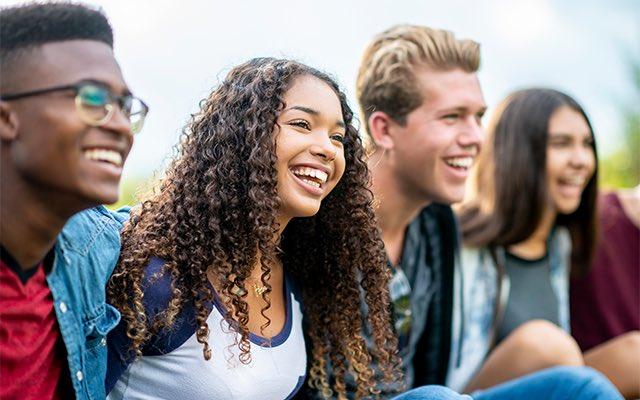 Four young people sit and laugh together on a bench. 