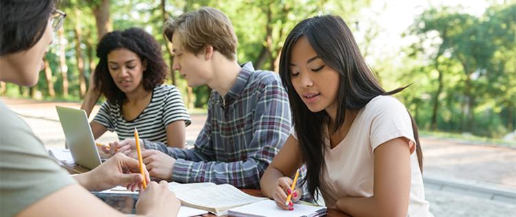 A group of four teens sitting at a table doing school work.